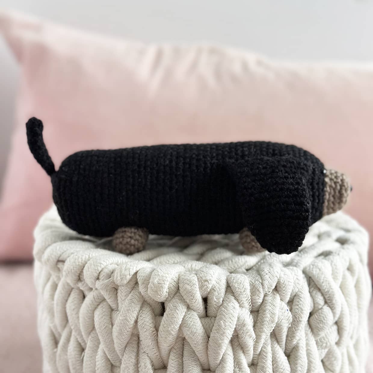 Black knit dog toy on a textured blanket with a pink pillow in the background