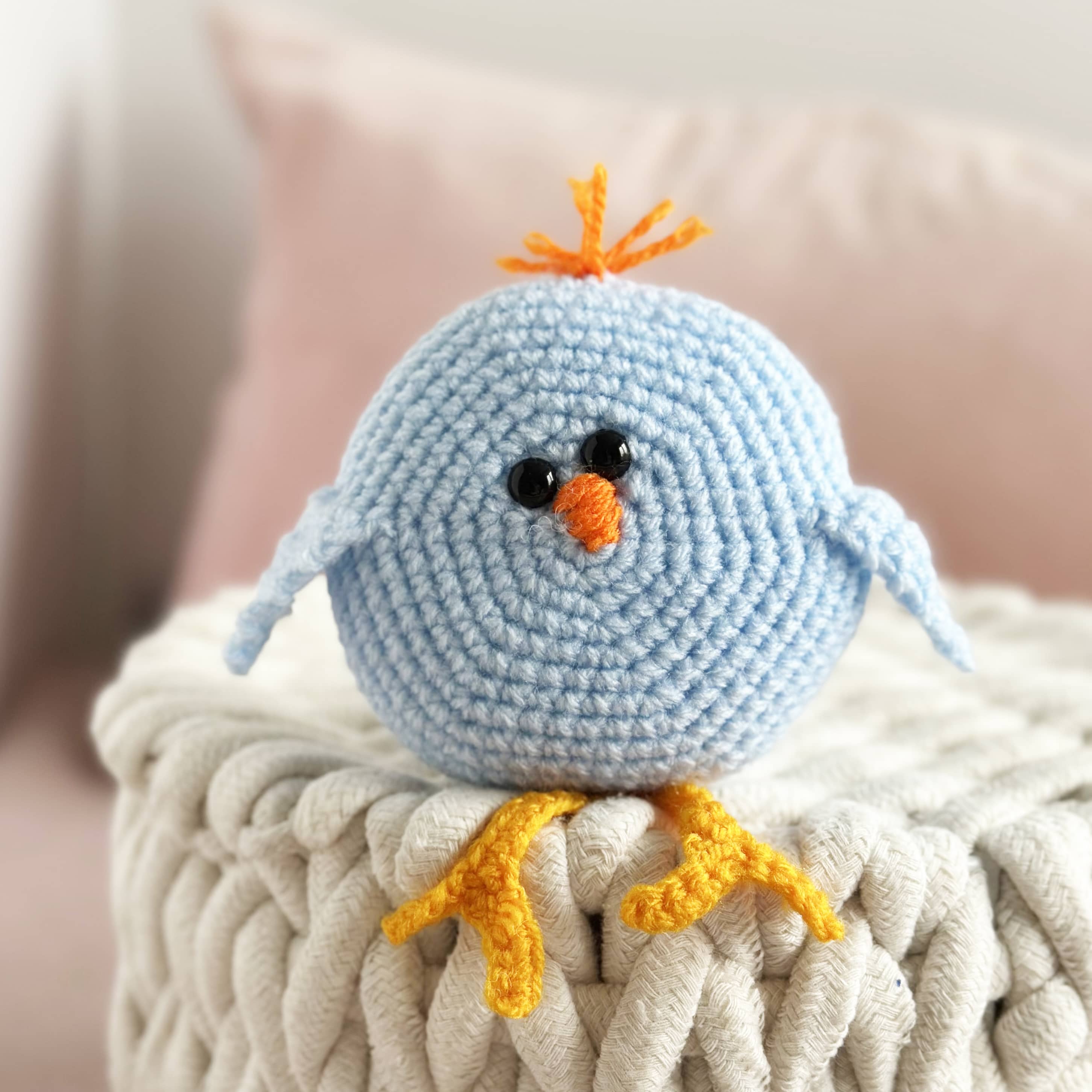 Crocheted blue bird toy with orange beak and feet on a textured surface.