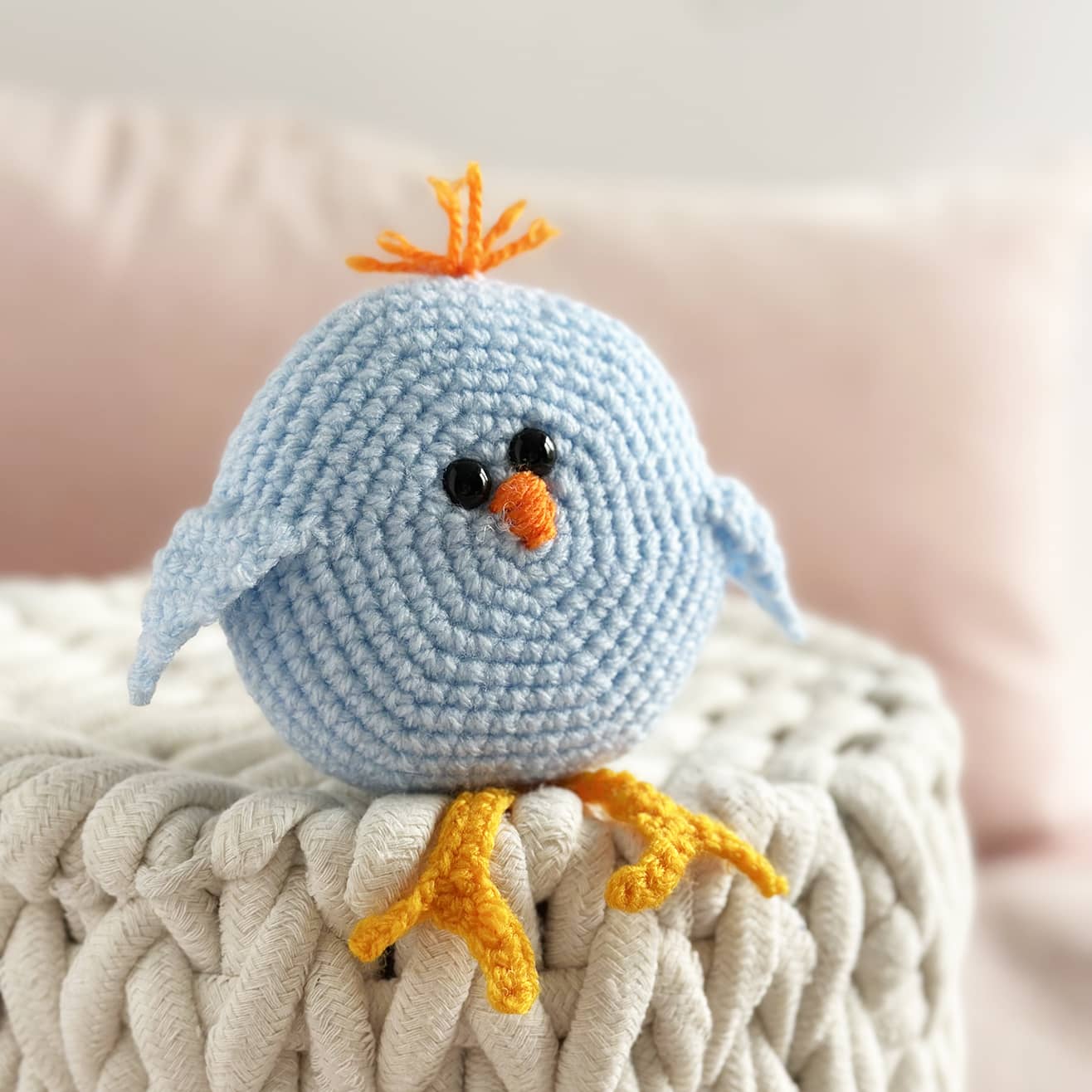 Crocheted blue bird toy with orange beak and feet on a textured surface