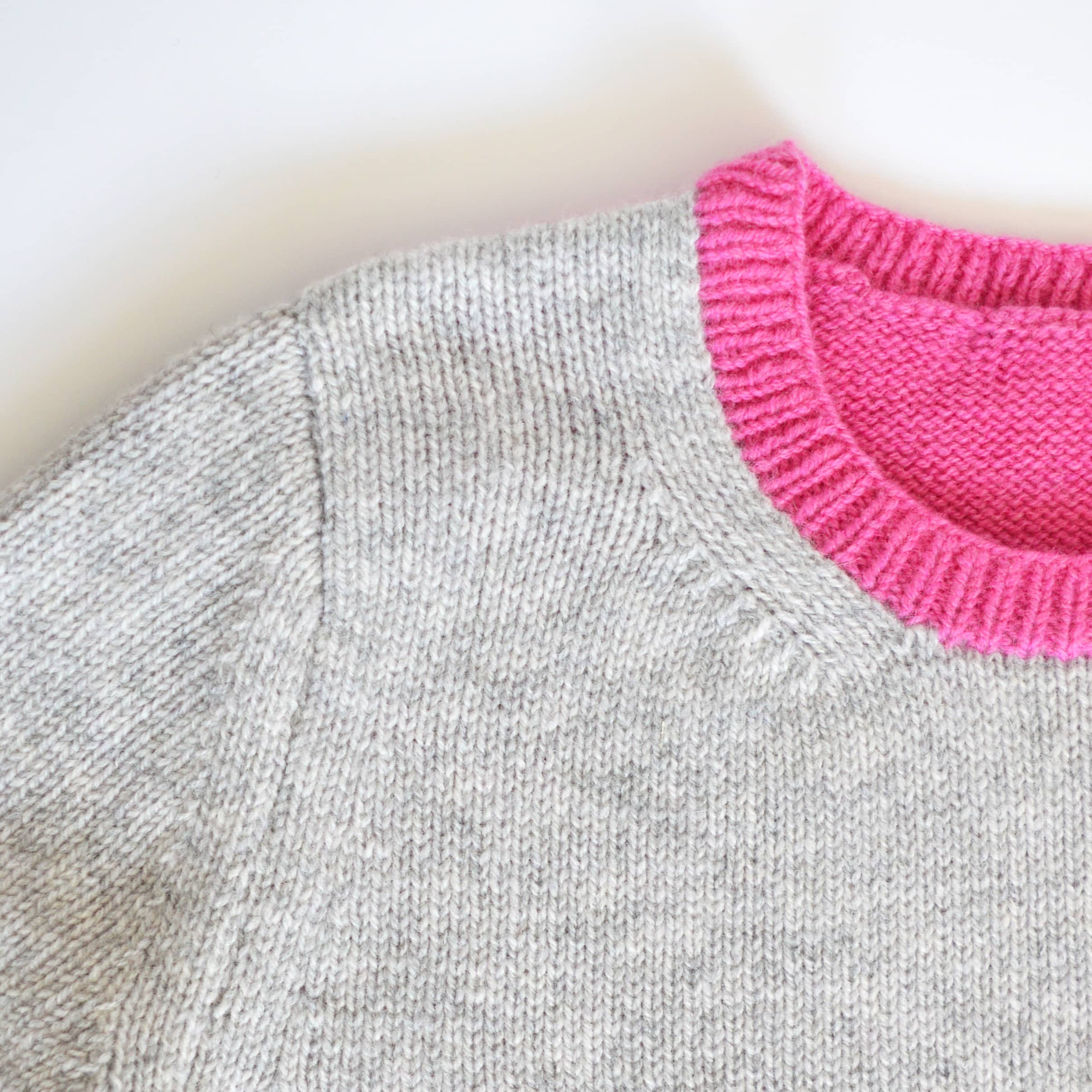 close up of neckline from knitting pattern, sweater knitting pattern, jumper knitting pattern. Grey and bright pink jumper