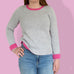 woman wearing modern knitting pattern jumper, knitting kit.  grey marl yarn and bright pink sweater knitting pattern