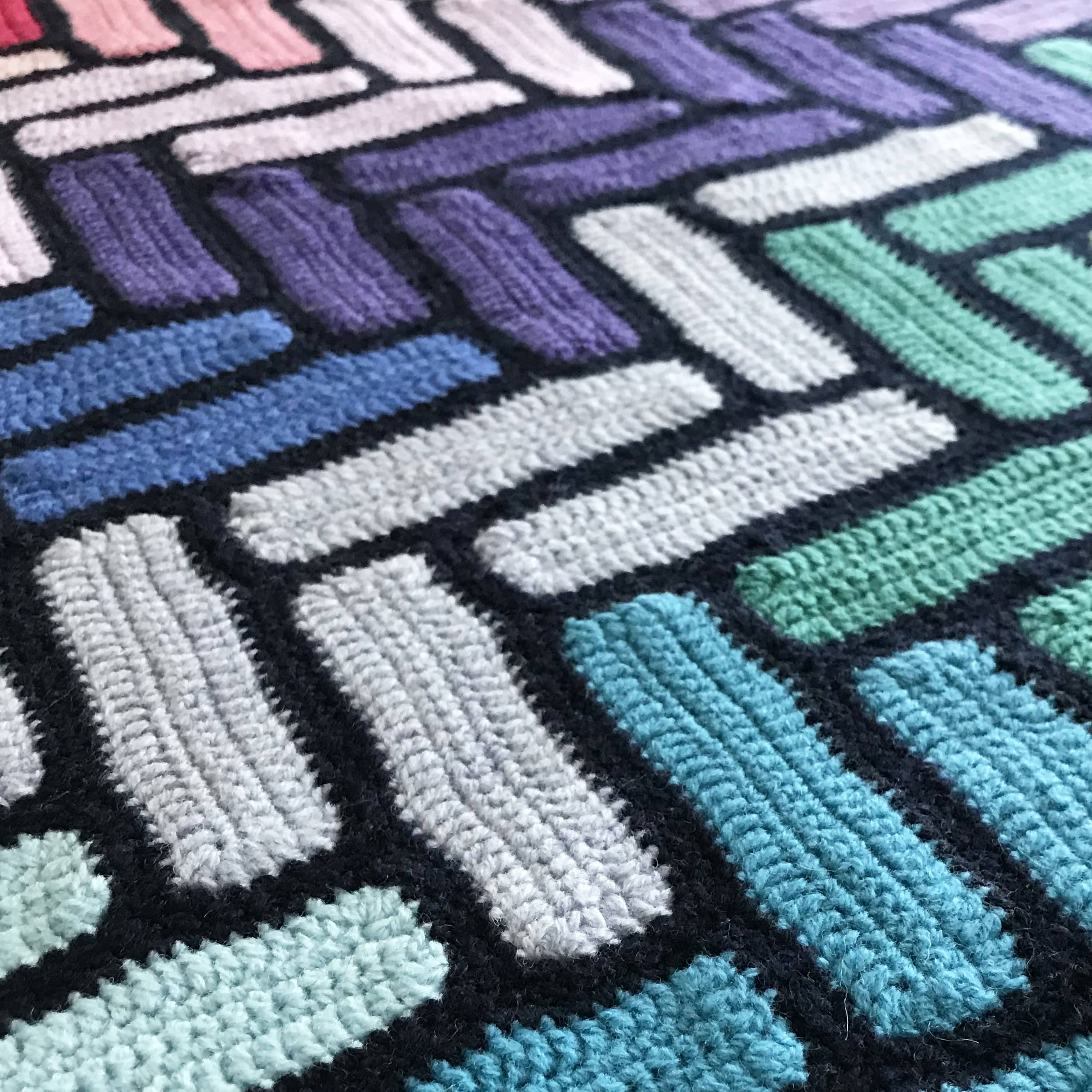 close up of granny square blanket using rectangles in blue green and purples