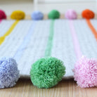 close up of pom pom and stripe crochet blanket kit