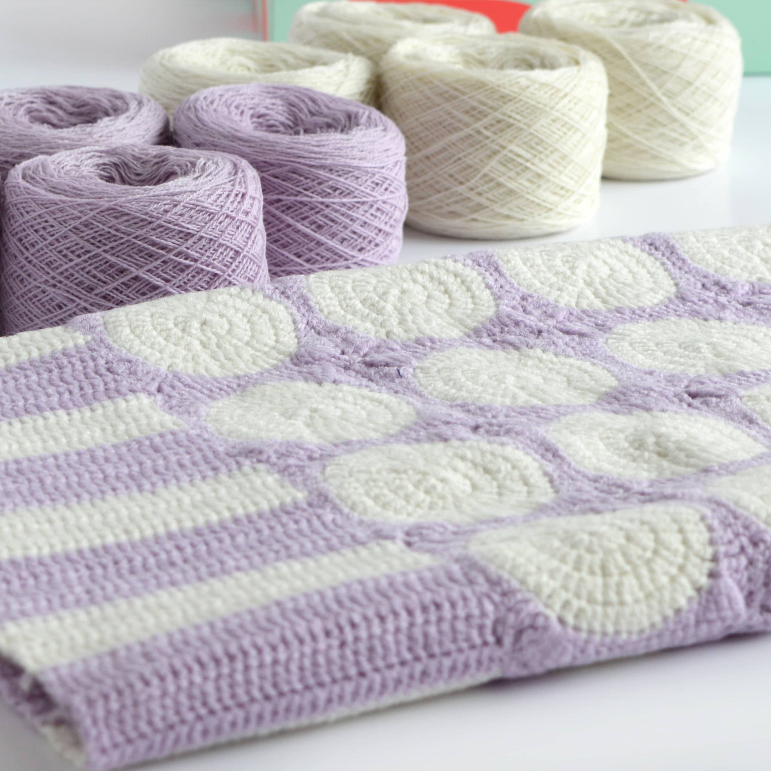 lilac and white granny square blanket on table showing yarn and box