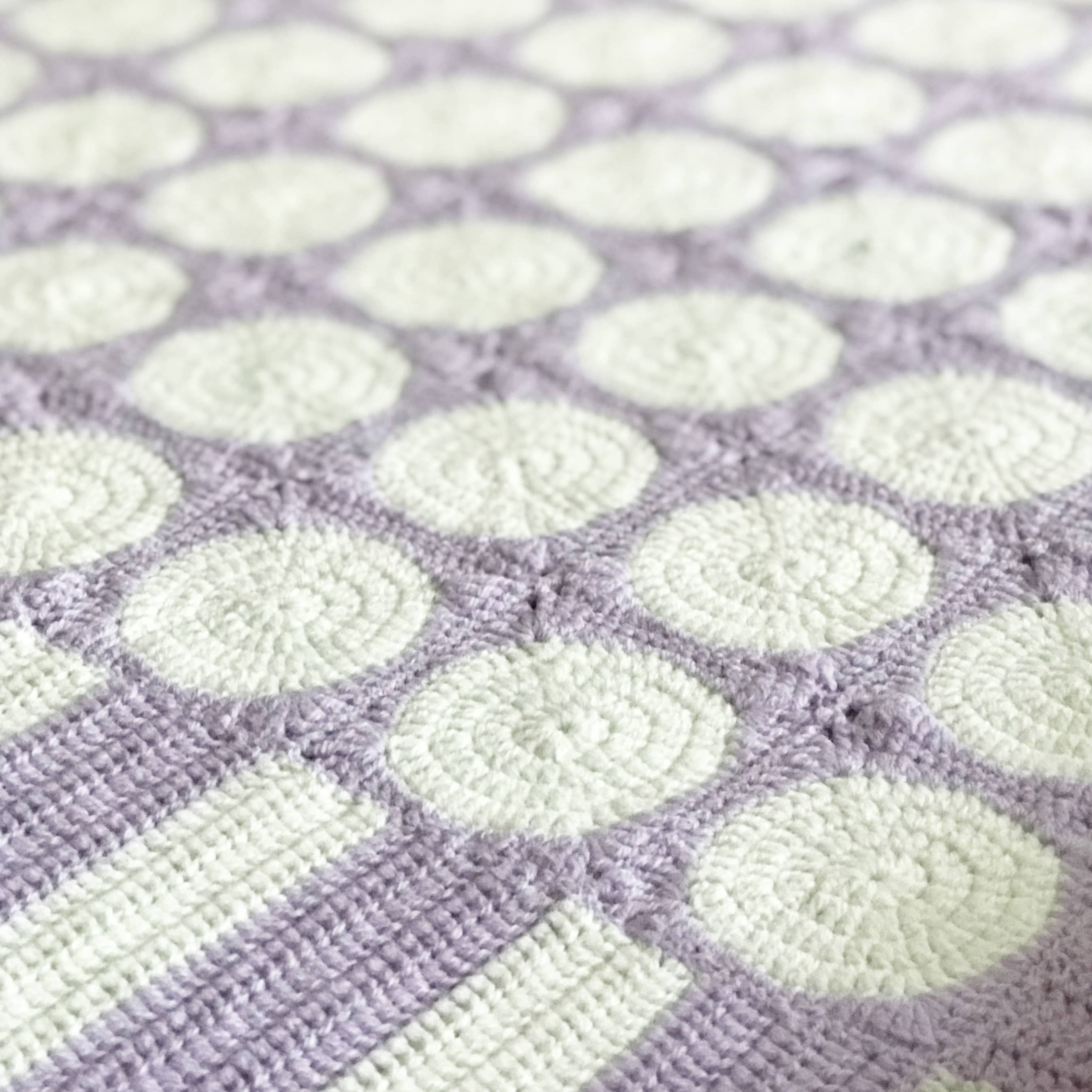 granny square blanket in pastel colours close up on table.