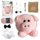 Pink crochet pig with yarn, needles, and other crafting supplies on a white background
