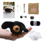 Crocheted dachshund toy with yarn, needles, and packaging on a white background