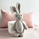 Crocheted bunny toy on a bed with pink pillows and a textured white box.