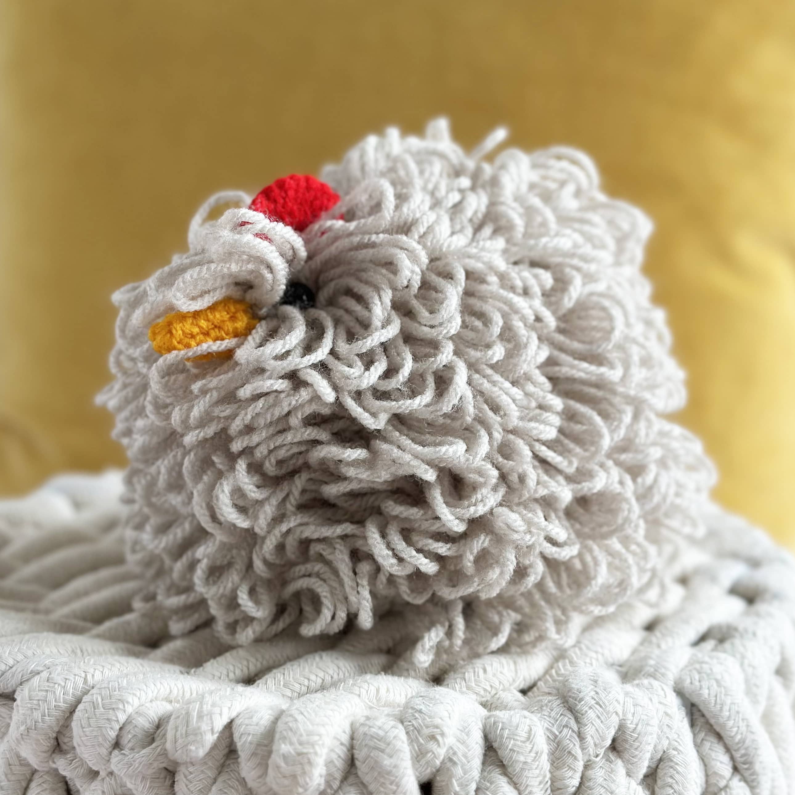 Knitted chicken toy with a red comb on a textured surface