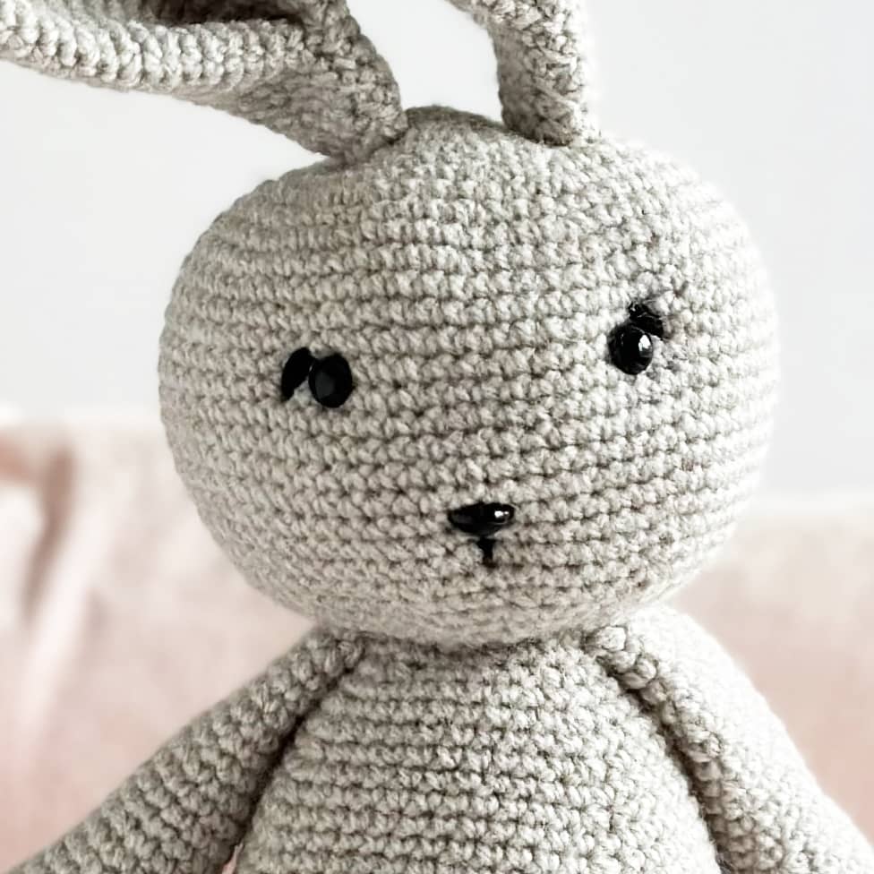 Close-up of a crocheted gray bunny toy with a blurred background