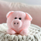 Pink crochet pig toy on a textured surface with a blurred background