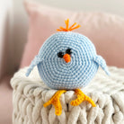Crocheted blue bird toy with orange beak and feet on a textured surface.