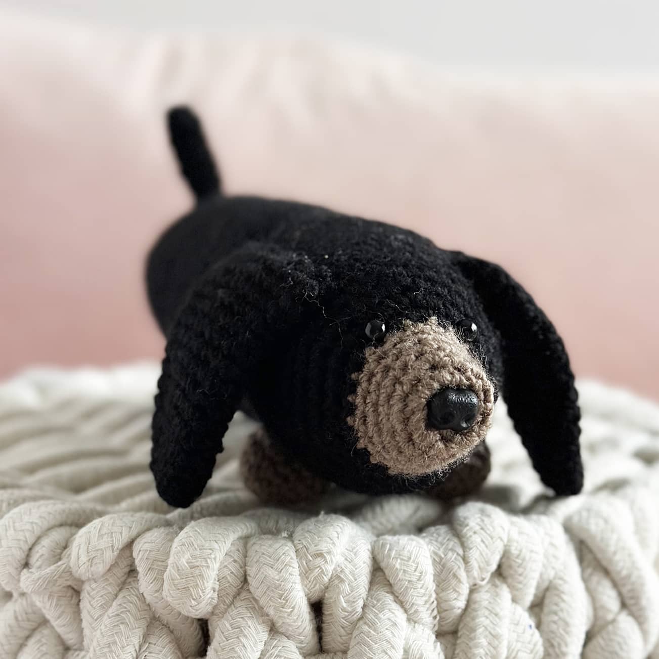 Crocheted black dog toy on a textured surface with a pink background