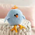Crocheted blue bird toy with orange beak and feet on a textured surface